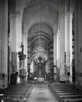 Vue intérieure d'une église baroque, avec une nef à hautes colonnes menant vers le maître-autel.