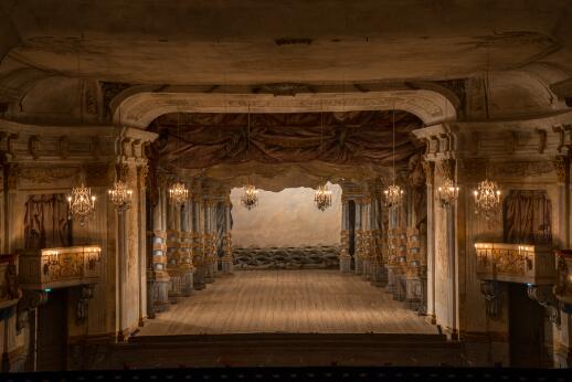 Salle de théâtre historique avec scène en bois, décor peint en perspective et loges richement ornées.