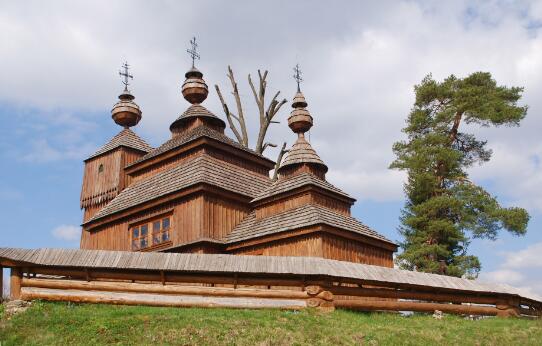 Vue extérieure d'une église en bois de rite oriental, à trois coupoles, entourée d'une palissade.