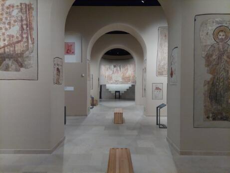 Galerie de musée présentant des fragments de peintures murales anciennes disposés le long d'un parcours voûté.