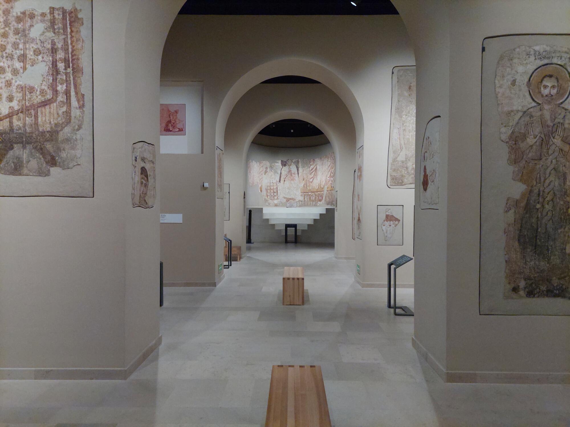 Preview of: Faras Gallery Galerie de musée présentant des fragments de peintures murales anciennes disposés le long d'un parcours voûté.
