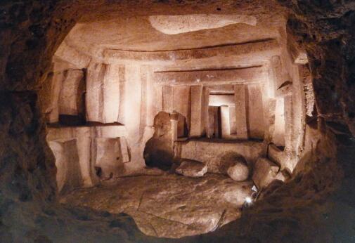 Intérieur d'un hypogée rupestre à chambres funéraires creusées dans la roche, avec piliers, linteaux et ouvertures taillés imitant une architecture monumentale.