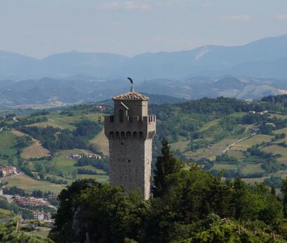Tour médiévale fortifiée dominant un promontoire rocheux, entourée d'un paysage vallonné.