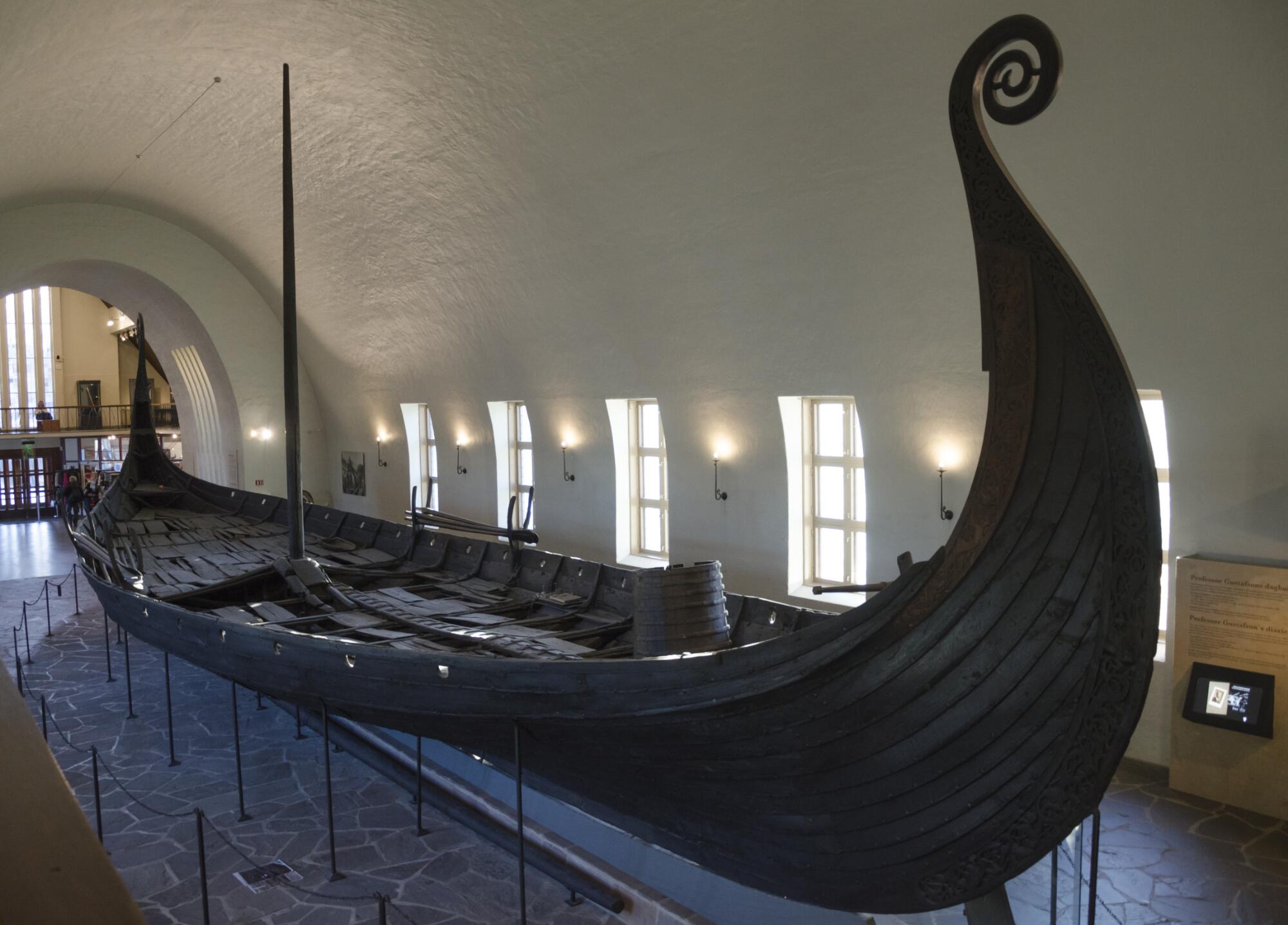 Preview of: The Oseberg Ship Navire viking en bois exposé dans un musée, caractérisé par sa coque élancée et sa proue sculptée recourbée.