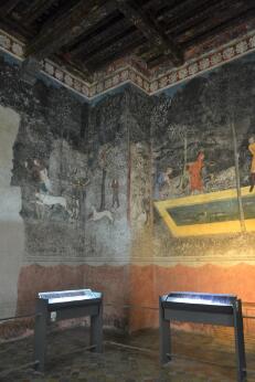 Salle ornée de fresques murales représentant des scènes de chasse et un jardin, avec plafond à poutres apparentes.
