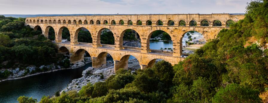 Vue panoramique du pont du Gard, aqueduc romain monumental à trois niveaux d'arches enjambant la rivière Gardon au milieu d'un paysage boisé.