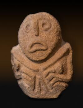 Petite sculpture anthropomorphe en pierre, au visage stylisé et aux bras repliés, caractéristique de l'art préhistorique.