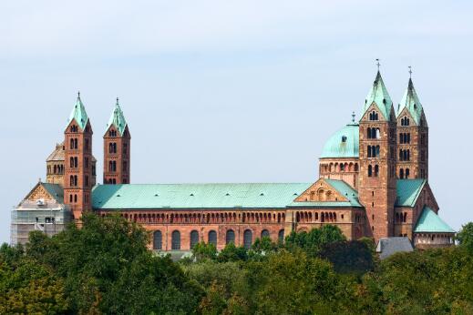 Vue extérieure d'une cathédrale romane monumentale, reconnaissable à ses quatre tours, son transept à coupole et ses façades en grès rouge.