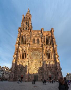 Vue extérieure de la façade occidentale d'une cathédrale gothique, dominée par une haute flèche, une grande rosace et un portail richement sculpté.