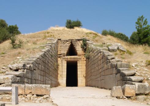 Entrée monumentale d'une tombe à tholos mycénienne, composée d'un long couloir d'accès (dromos) bordé de murs en grands blocs de pierre menant à un portail trilithe ouvrant sur une chambre funéraire souterraine.