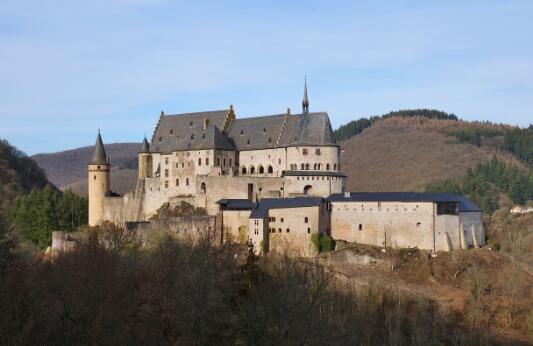 Château fort médiéval en pierre, doté de tours et de remparts, construit sur un promontoire rocheux dominant une vallée boisée.