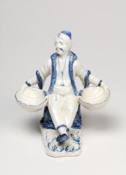 Figurine en faïence représentant un homme oriental assis tenant deux coquilles.