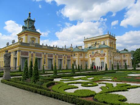 Vue extérieure d'un palais baroque entouré de jardins à la française, caractérisés par des parterres géométriques, des haies taillées et des statues ornementales.