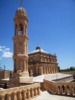 Vue extérieure d'une église en pierre de style médiéval, accompagnée de son clocher indépendant richement sculpté, caractéristique de l'architecture chrétienne du Proche-Orient.