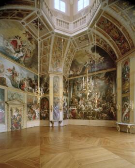 Vue intérieure d'une salle d'apparat ornée de vastes peintures murales et de plafonds décorés, avec un parquet en bois, des lustres en cristal et une architecture baroque richement sculptée.
