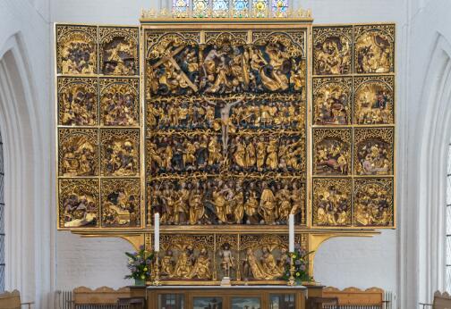 Grand retable sculpté et doré composé de nombreuses scènes et figures en relief, installé au fond d’une église entre deux hautes fenêtres.