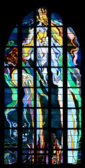 Vitrail représentant une figure divine aux longs cheveux blancs, levant une main en geste de bénédiction, dans une composition aux lignes ondoyantes et aux couleurs vives de style Art nouveau.