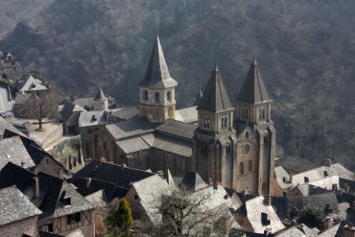 Édifice religieux représentant une église abbatiale romane à trois tours, intégrée au cœur d'un village historique.