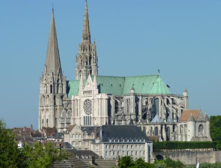 Vue extérieure d'une cathédrale gothique en pierre, dominée par deux flèches de hauteurs différentes.